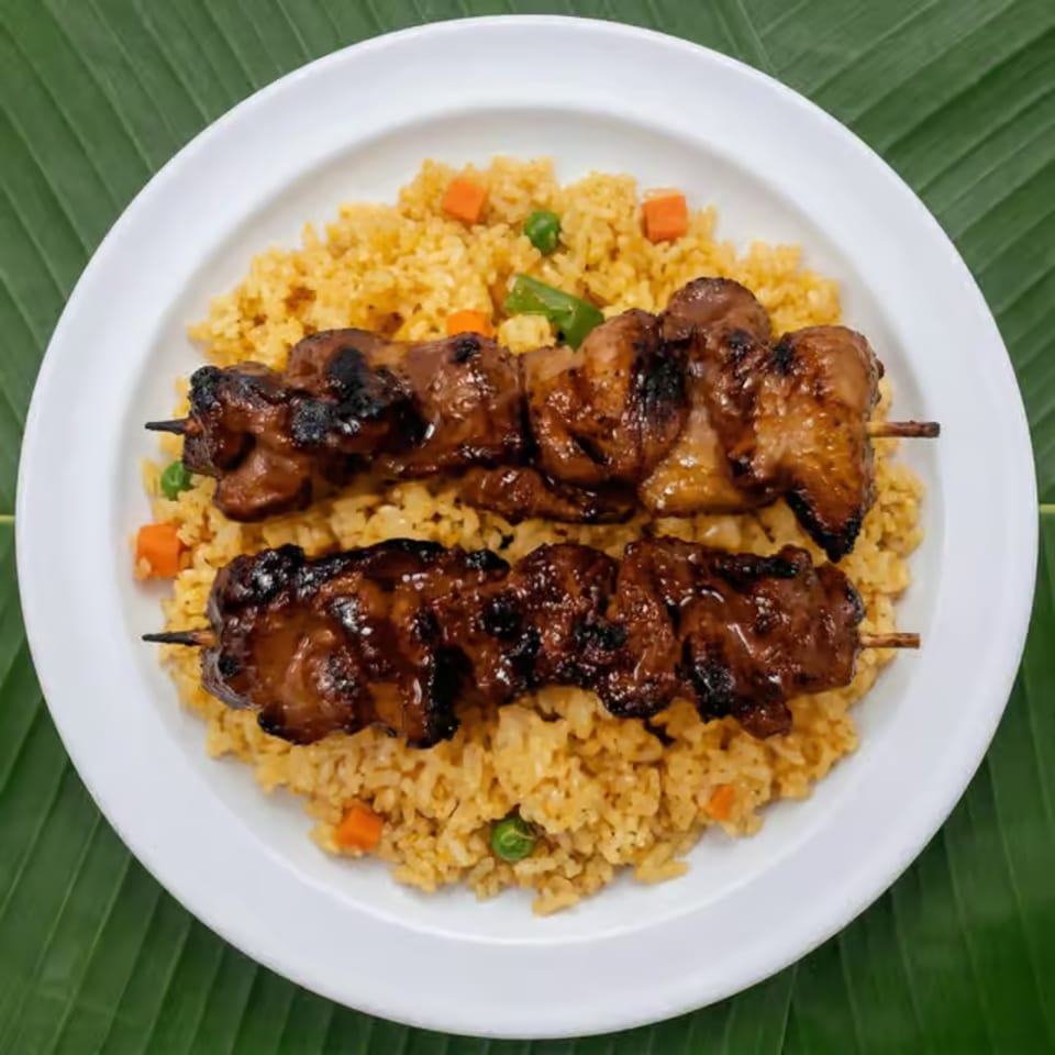Two skewers of grilled chicken over a bed of yellow rice with peas and carrots on a white plate.